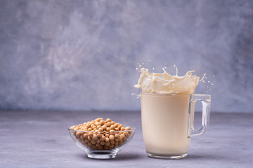 On gray background rustic, the glass of soy milk with splash and yellow soy beans