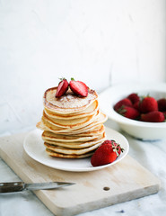 breakfast a stack of lush pancakes with strawberries on a white plate on a light background