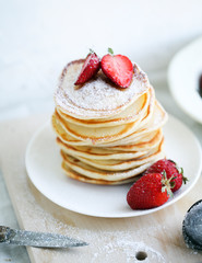 breakfast a stack of lush pancakes with strawberries on a white plate on a light background