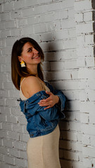 brunette girl in a green jacket and bra stands near the white brick wall