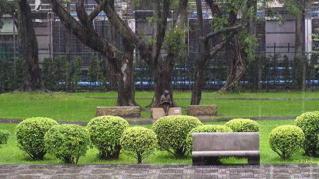 Heavy rain is falling on the pavement and modern wooden bench outdoors in the park. front view
