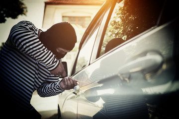 Car theft, Bandits in the black dress are using a screwdriver to unlock the car. Social crime.