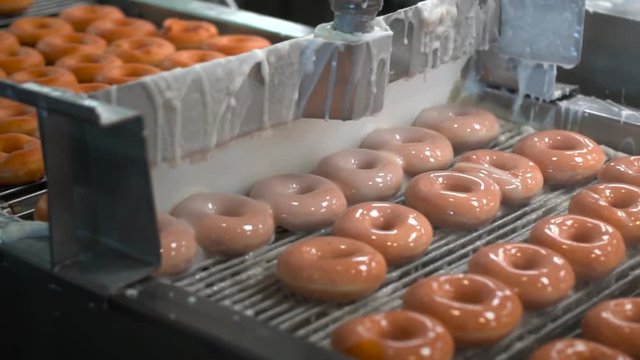 This video shows a fresh batch of donuts being glazed by machine in donut f...