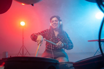 Emotions, music, hobbies and people concept - young woman playing the electronic drum set in studio