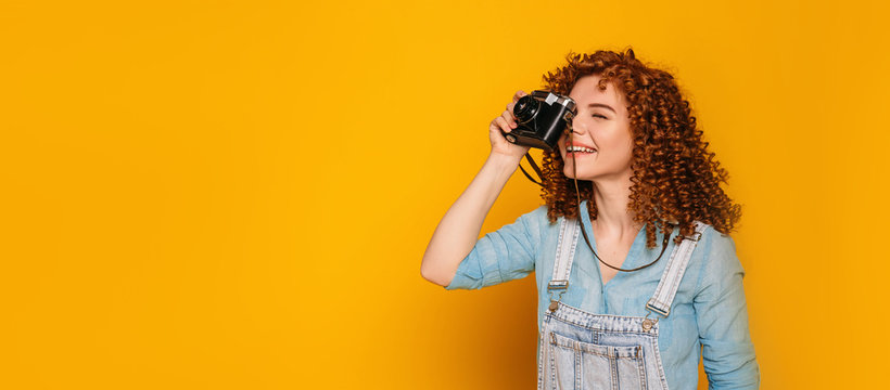 Take a good shoot. Positive curly haired teenage girl make a photo on yellow background.