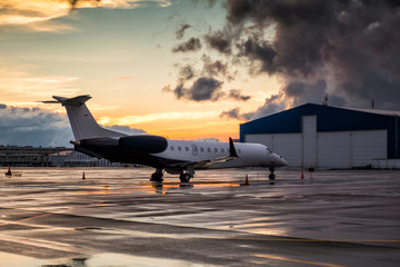 Business jet at sunset after the rain on the airport apron near the hangar - obrazy, fototapety, plakaty