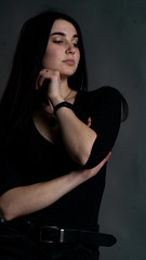 Portrait of young brunette woman sitting on high wooden chair with crossed legs. Fashionable stylish girl wearing wide leg pants. Studio shoot on gray background