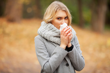 Girl sneezing in tissue. Young woman blowing her nose on the park. Woman portrait outdoor sneezing because cold and flu