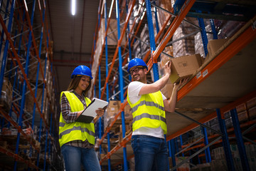 Warehouse workers working together on relocating boxes in warehouse. Female worker with checklist and telling where to move the package.