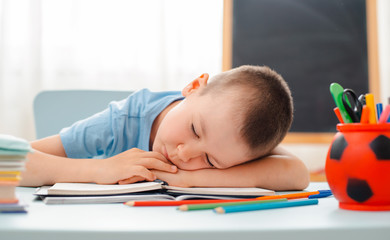 Naklejka premium school boy sitting at home classroom lying desk filled with books training material schoolchild sleeping lazy bored