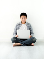 Smart Asian preteen boy using  laptop and sitting sitting on the floor.