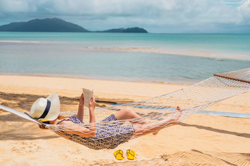 Woman reading a book on hammock beach in free time summer holiday - Powered by Adobe