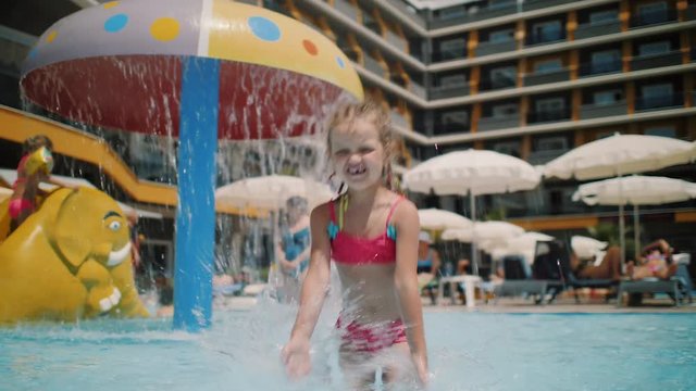 Cute little girl having fun and splashing in the water in the paddling pool with children's entertainment. Enjoying a hot summers day at the resort. 4k slow motion.