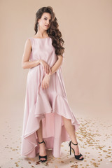 Fototapeta premium Beautiful girl in evening elegant dress posing on paper beige studio background full length portrait
