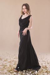 Beautiful girl in evening elegant dress posing on paper beige studio background full length portrait