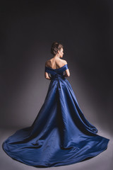 Beautiful woman in elegant blue dress with plume posing on dark background. Back view