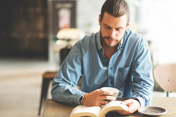 Male freelancer in blue shirt reading a book. - Powered by Adobe