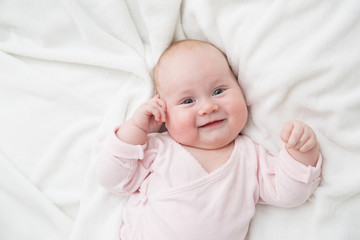 Newborn baby girl posed on her back, on blanket of fur, smiling looking at camera