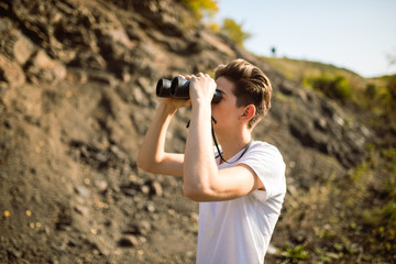 Young man holding a binoculars looking on top of mountain