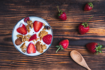 Top view bowl of fresh berries and yogurt mixed with fresh strawberries on a wooden table.
