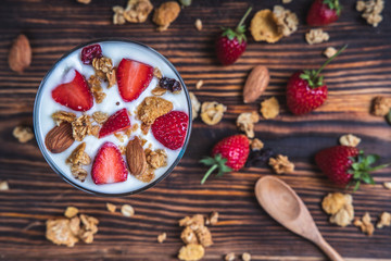 Top view bowl of fresh berries and yogurt mixed with fresh strawberries on a wooden table.