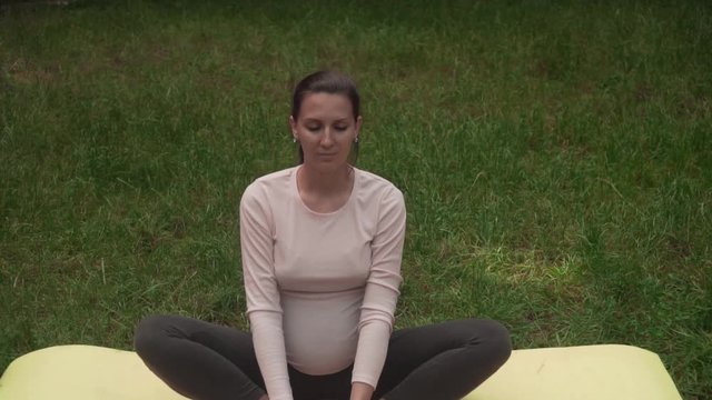 A pregnant woman practices yoga in the park on a rug, doing the asd baddha konasana, butterfly pose. Relaxation and being in asana.