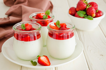 Dietary creamy yogurt panna cotta with fresh strawberry sauce in glass jars.