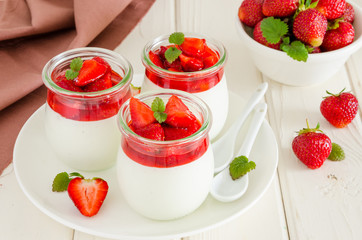 Dietary creamy yogurt panna cotta with fresh strawberry sauce in glass jars.