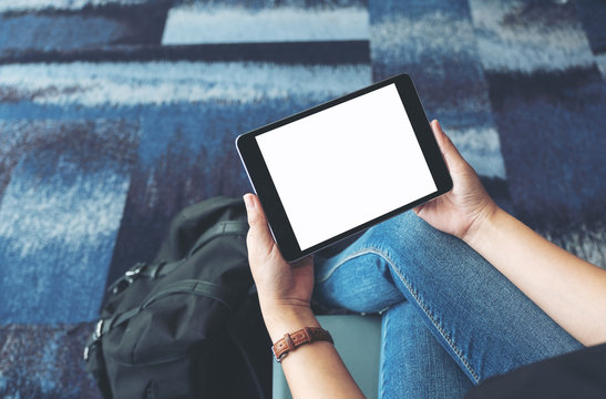 Mockup image of a woman's hands holding and using black tablet pc with blank white screen while sitting in the airport