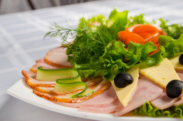 banquet cutting with ham, meat delicacies, cheese, sausage smoked, olive, lettuce and tomato on white dish