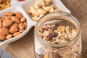 Granola cereal flakes with dried fruit, nuts in green bowl on gray wooden table.