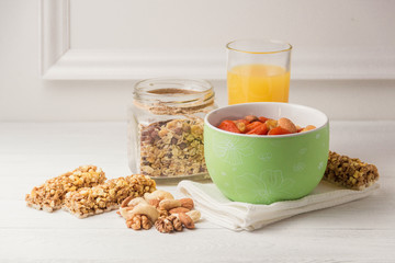 Granola cereal flakes with dried fruit, nuts in green bowl on white wooden table.