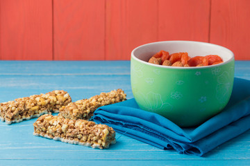 Granola cereal flakes with dried fruit, nuts in green bowl on blue wooden table.