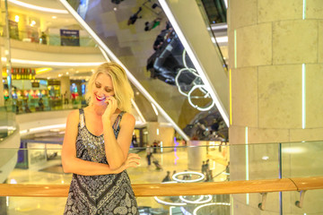 Young woman in Singapore luxury shopping mall on Orchard Road, talking with mobile phone. Happy caucasian lifestyle lady shopper using a smartphone in a mall background.