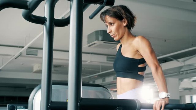 Athletic woman in sportswear is doing push-ups on parallel bars in gym. Sport and bodybuilding concept.
