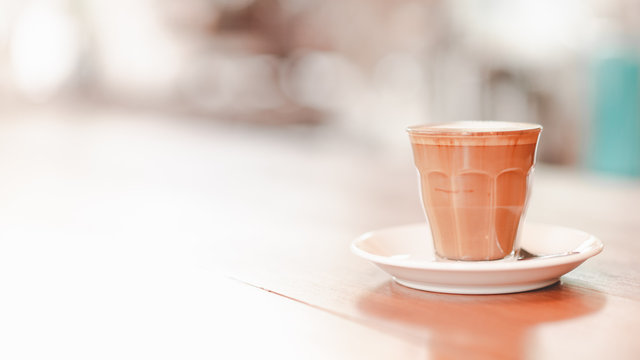 small cup of piccolo latte served on wooden table with copy space on left, retro tone
