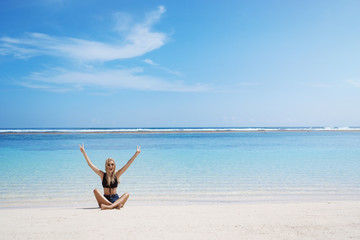 Fototapeta na wymiar Woman screams happily sitting crossed legs sunny sandy beach lift hands show peace victory sign grinning delighted enjoy summer vacation seaside resort, perfect tourist tour holiday, relaxing excited