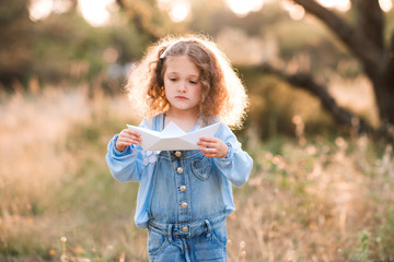 Cute kid girl 3-4 year old making paper origami ship outdoors. Childhood. Pre shcool.