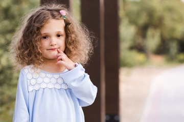 Pretty baby girl 3-4 year old with curly blonde hair posing outdoors in park. Summer time.