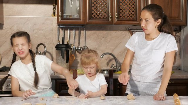 Portrait of playful mom and daughters throw flour to each other while cooking in the kitchen. Family cooking at home, funny pastime.