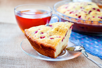 Piece of cowberry pie on glass plate and cup of tea