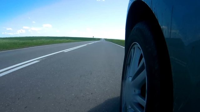 Car stops on a roadside of a highway in a sunny summer day. Camera is mounted on a side of the car with view of a rolling tire