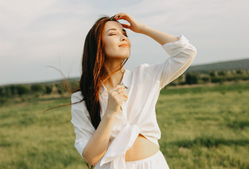 Portrait of beautiful carefree long hair girl in white clothes on field at sunset. Sensitivity to nature concept