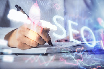 Double exposure of woman's hands making notes with SEO icon. Concept of Search engine optimization