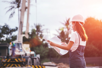 Portrait of engineer woman looking for construction, Asian female architect with blueprints standing on the background of construction work, Engineering and architecture concept.