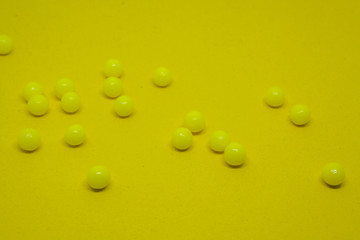 Scattered chaotically yellow dragee on a yellow background close-up.