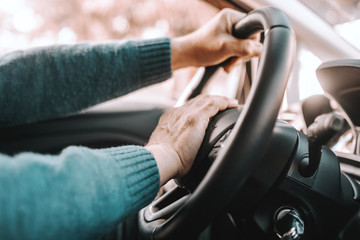 Close up of senior man driving his car. One hand on steering wheel and other on horn.