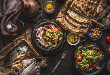 Salad bowl with backed fish and homemade bread on on dark rustic table, top view. Mediterranean lunch or dinner. Healthy food