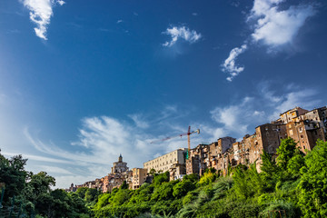 Fototapeta na wymiar A view of the city of Zagarolo, with the houses built sheer above a tuff hill. Above the roofs, the dome of the church of San Pietro and a crane emerge. The valley full of trees. Rome, Lazio
