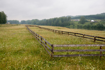 Fototapeta premium Heavy grey clouds in the cold autumn sky over village. Old local farm and low fences in the mountains and fields. Travelling on the suburb roads. Cows and sheep are pasturing 